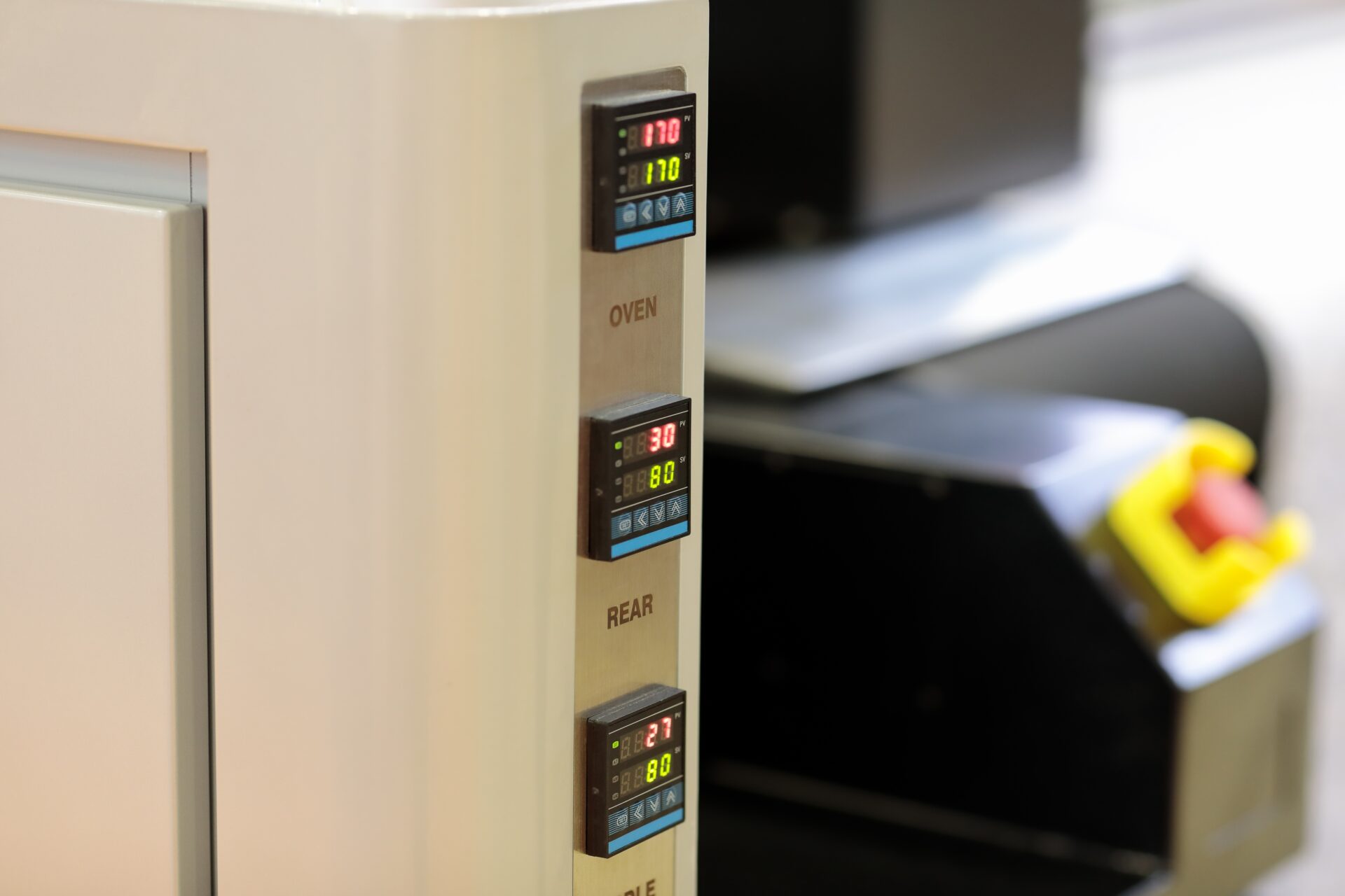Digital temperature controllers on a control panel of industrial textile printing machine. Selective focus.